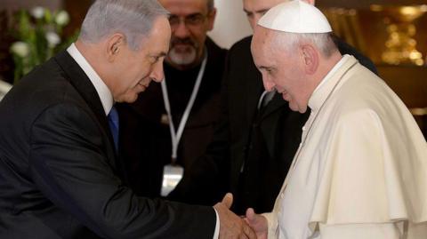 Prime Minister Benjamin Netanyahu, wearing a black suit, and Pope Francis, wearing his white papal garments, shake hands as they meet in Jerusalem in 2014