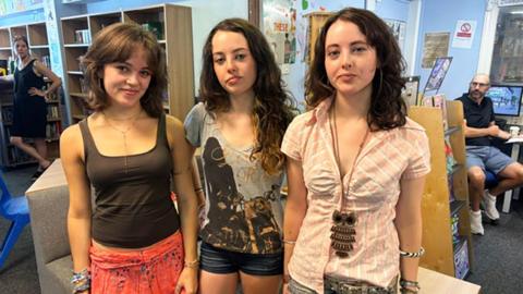 Triplets Scarlett, Tabby and Grace Taylor stand in a row and face the camera