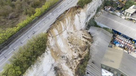 An aerial view of a landslip on a road which collapsed onto a building.
