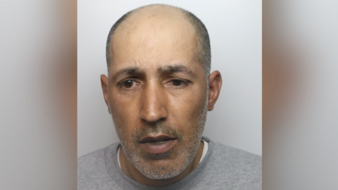 A mugshot of Rahman, who is unshaven, balding and wearing a grey jumper.