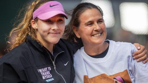 Mirra Andreeva puts an arm around Conchita Martinez as both smile. Andreeva is wearing a dark jacket that has the slogan 'I want to thank myself - Mirra'