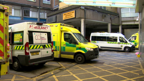 The exterior of the ambulance bay of the Royal Victoria Hospital in Belfast. There are multiple ambulances parked outside the brown exterior door.