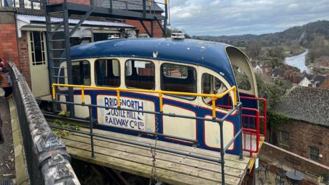 A cliff railway carriage which is white and blue. There is a sign on the side that reads "Bridgnorth Castle Hill Railway co limited".