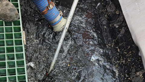 A large cess pit being removed by an industrial hoover, whilst being broken up by a metal pole.
