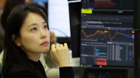 A currency dealer with a thoughtful look as she analyses charts displayed on monitorsin a foreign exchange dealing room at the Hana Bank headquarters in Seoul