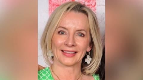 Sam Phipps smiles while wearing a green dress, necklace and flowery earrings. She has blond hair