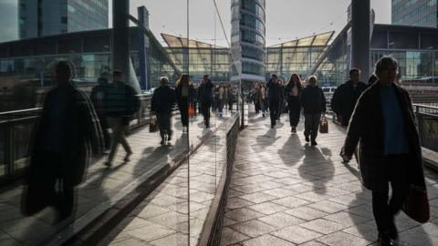 Commuters walking in shadow next to a glass building.