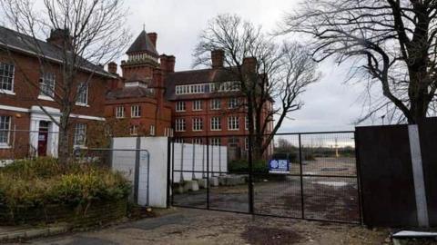 The view of the hotel building from outside its car park. It is a Georgian-looking building with red bricks and white pillars either side of the front door. There are several trees in the car park.