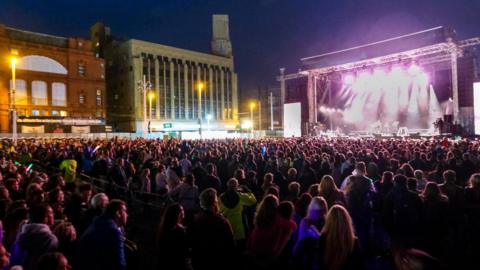 A crowd of people looking towards a stage with purple lighting at a previous switch-on event