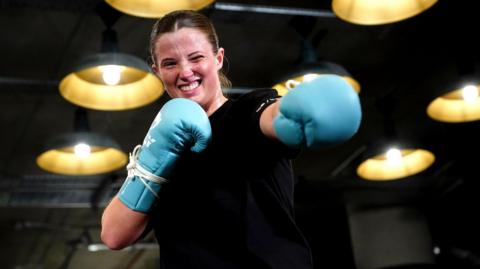 Fran Hennessy, known as the Billion Dollar Baby, punches the air wearing sky blue gloves with a smile on her face.