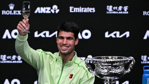 Carlos Alcaraz lifts a glass of champagne during a press conference