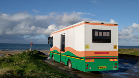 A picture of the coach in which the library will be housed. It's parked on the side of the road looking out to sea. 