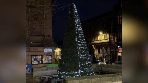 A Christmas tree with only one side covered in lights.