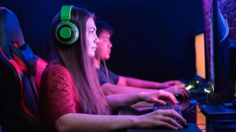 Boy and girl playing computer games together under neon lighting.