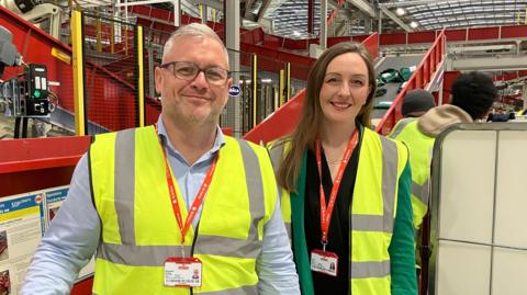 Alex Grieves and Jenny Hall in hi-visibility jackets pose for a photo at the parcel facility in Daventry.