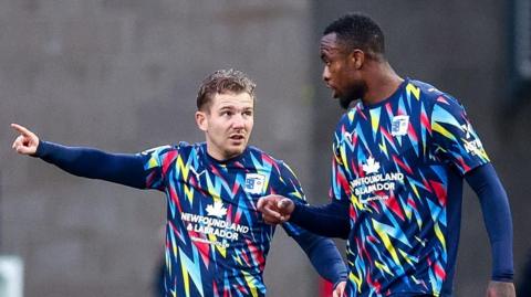 Ben Whitfield (left) pointing with his right hand to team-mate Rekeem Harper during Barrow's away game at Swindon