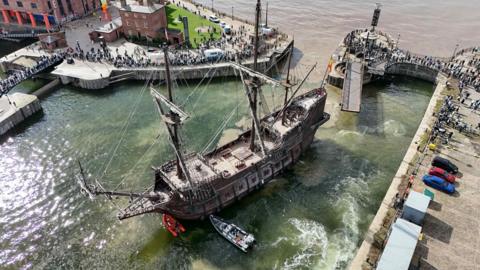 An aerial view of the 160ft (48m) galleon which has six decks. Made from iroko and pine, its seven sails measure nearly 1,000 square metres. There are crowds of people surrounding the ship as it is moored at Liverpool's Royal Albert Dock.