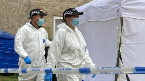 Two forensic investigators in white suits walking to the scene of the stabbing