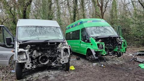 Two minibuses - one grey and one green - with their fronts missing.