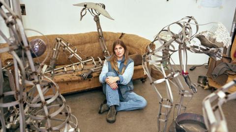 Kira Freije sitting in front of her artwork Unspeak the Chorus 