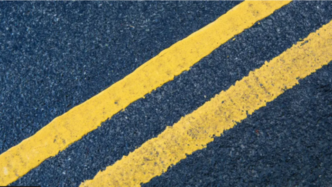 A double yellow line on a black tarmac road.