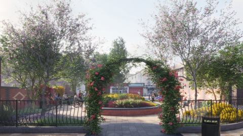 A floral archway leads into a paved area with a circular planted area with tress and shrubs either side
