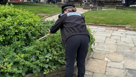 A female police officer looking inside a bush for a bladed weapon 