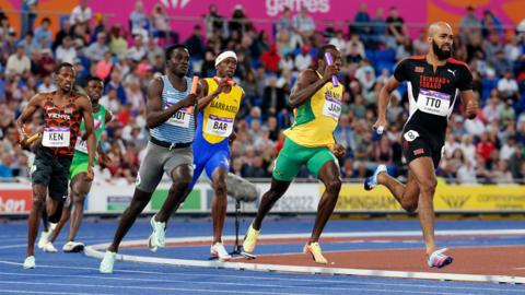 A relay race on the athletics track - six runners are visible, in various brightly coloured gear and the names of their countries on their tops.