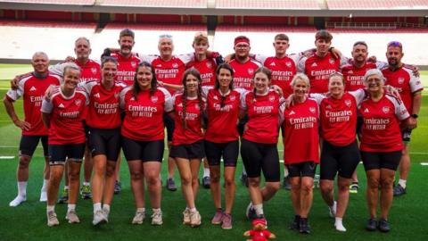 A group of people wearing arsenal t shirts posing pitch-side at the emirates stadium in London