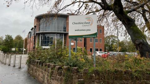 Cheshire East Council headquarters at Westfields in Sandbach. It's a large brick building with a glass wall on the first floor above its main entrance. 