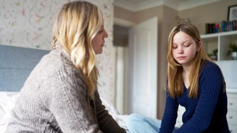 A frustrated mother talking to a sad teenage girl in a bedroom