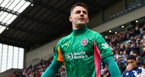 Wigan Athletic goalkeeper Sam Tickle walking out before an EFL football match, wearing a green goalkeeping top.