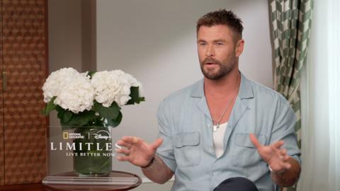 Chris Hemsworth wearing a blue shirt, he has a vase with white flowers to the side of him