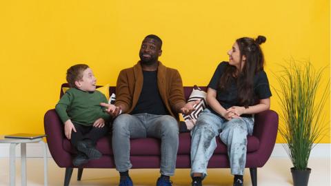 A boy, a man and a woman are sat on a sofa