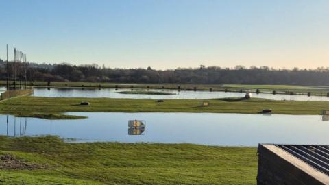 A grassy golf range with large areas flooded with signs marooned on their own in the centre of the water. 