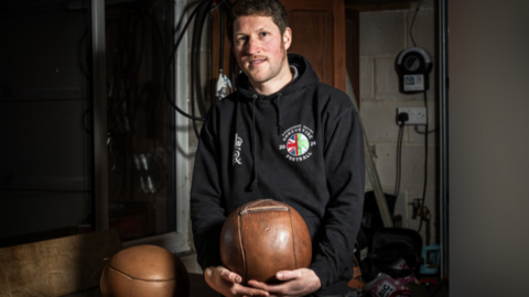 Carl Spencer stood holding a leather football wearing a black hoodie