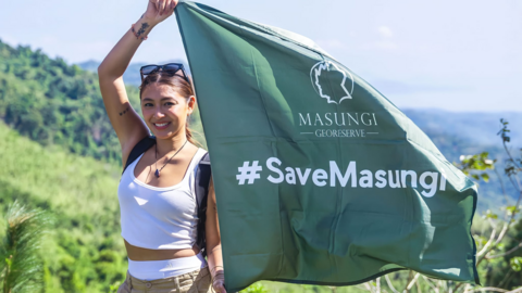 Filipino actress and singer Nadine Lustre holds a green flag with the hashtag #SaveMasungi on it, against a backdrop of lush rainforest