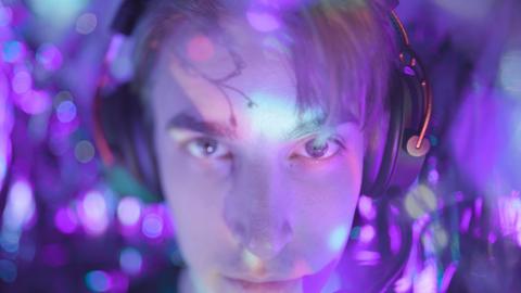 Face of a young man wearing a gaming headset, his face is lit in purple light