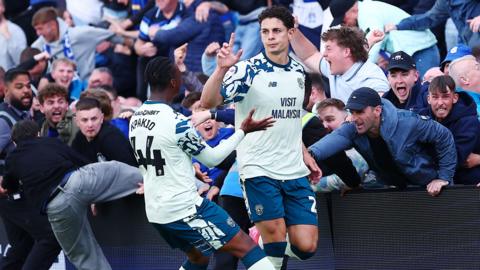 Yousef Salech celebrates a goal with Cardiff City fans behind him. Kapakio is to his side also celebrating