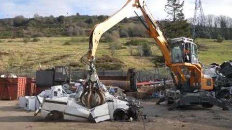 A white car being crushed in a yard