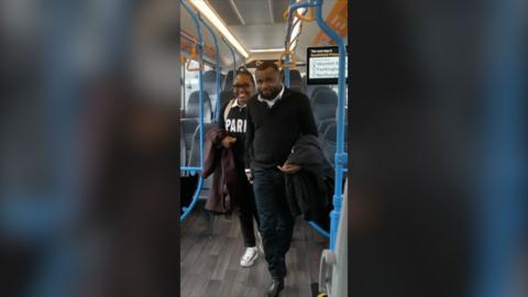 A man and a woman smile while walking through a bus