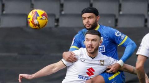 MK Dons' Scott Hogan and AFC Wimbledon's Ryan Johnson battle for the ball 