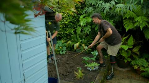 Young man with a prosthetic leg digs in a garden