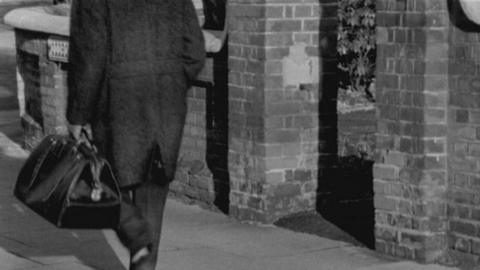 tv producer Paul Ferris walks along a street holding a travelling bag.