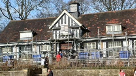 The Rose Garden Café in Graves Park, Sheffield, with customers queuing out of the door. Scaffolding surrounds the Tudor-style building.