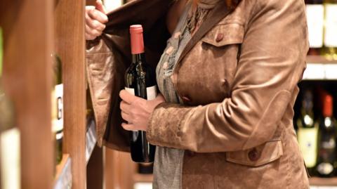 A woman stealing a bottle of wine in an off-licence.