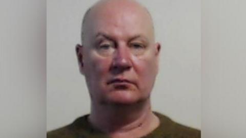 The mug shot of a bald white man with a ruddy face.