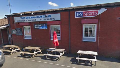 Street view image of Wilbraham Club on Geoffrey Street in Ribbleton. A red brick building with picnic benches outside. A banner says the name of a club and that a function room is available to hire. A Sky Sports poster is alongside it. 