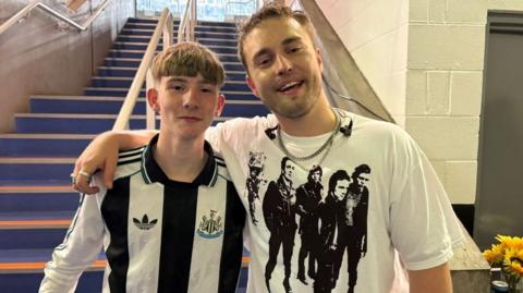 Joe Bartley and Sam Fender back stage at St James' Park. Fender has his arm around Joe who is wearing a Newcastle United shirt.