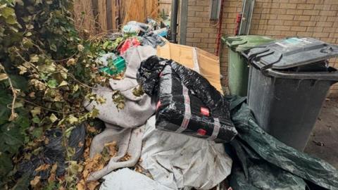 Piles of rubbish placed next to a green and a black bin.